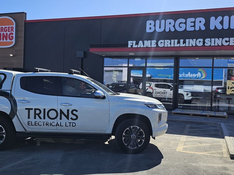 Trions Electrical utility vehicle parked outside a Burger King restaurant, with signage and reflection in the glass.