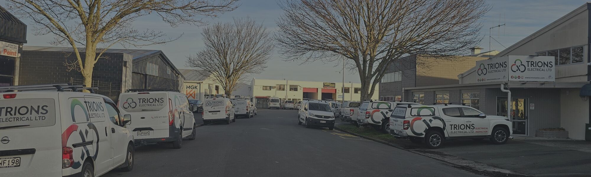 Two Trions Electrical team members standing between branded vans inside a large industrial facility.