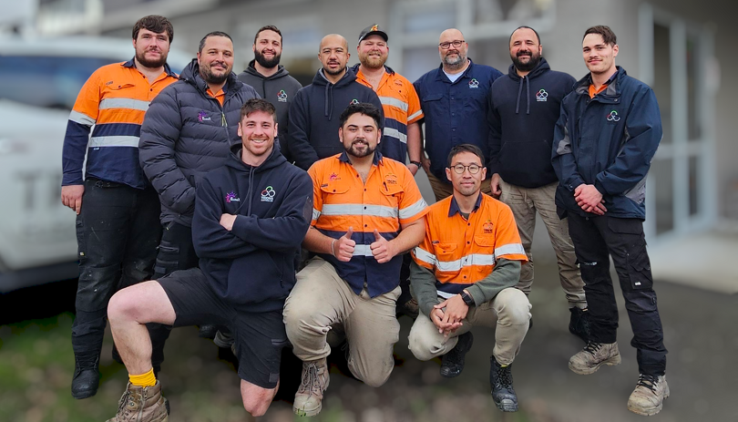 Trions Electrical team posing together outside a building, wearing high-vis orange and navy uniforms.