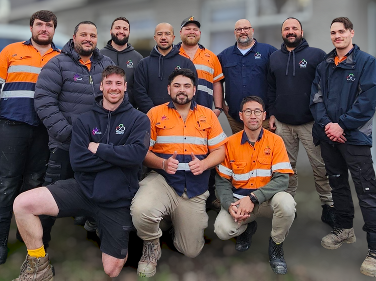 Trions Electrical team posing together outside a building, wearing high-vis orange and navy uniforms.